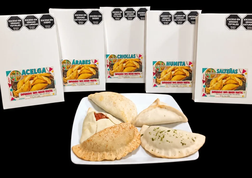 Las 5 variedades de empanadas veganas X+Vida en sus cajas (acelga, árabes, criollas, humita y salteñas) y un plato con empanadas horneadas